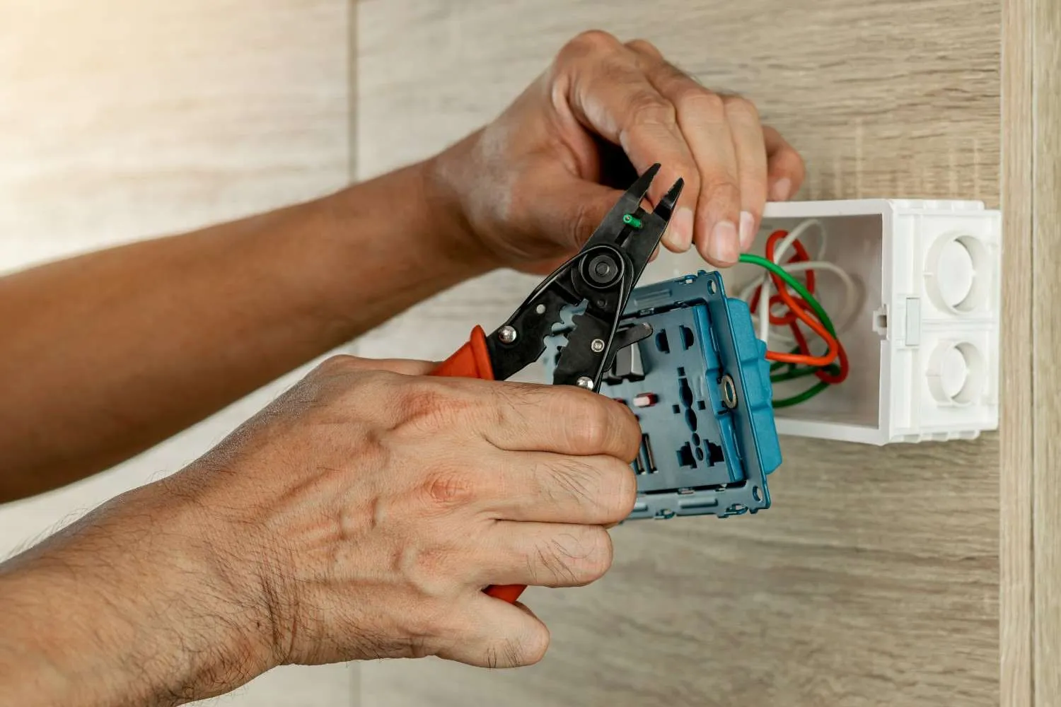 Hands stripping wires at a wall outlet box