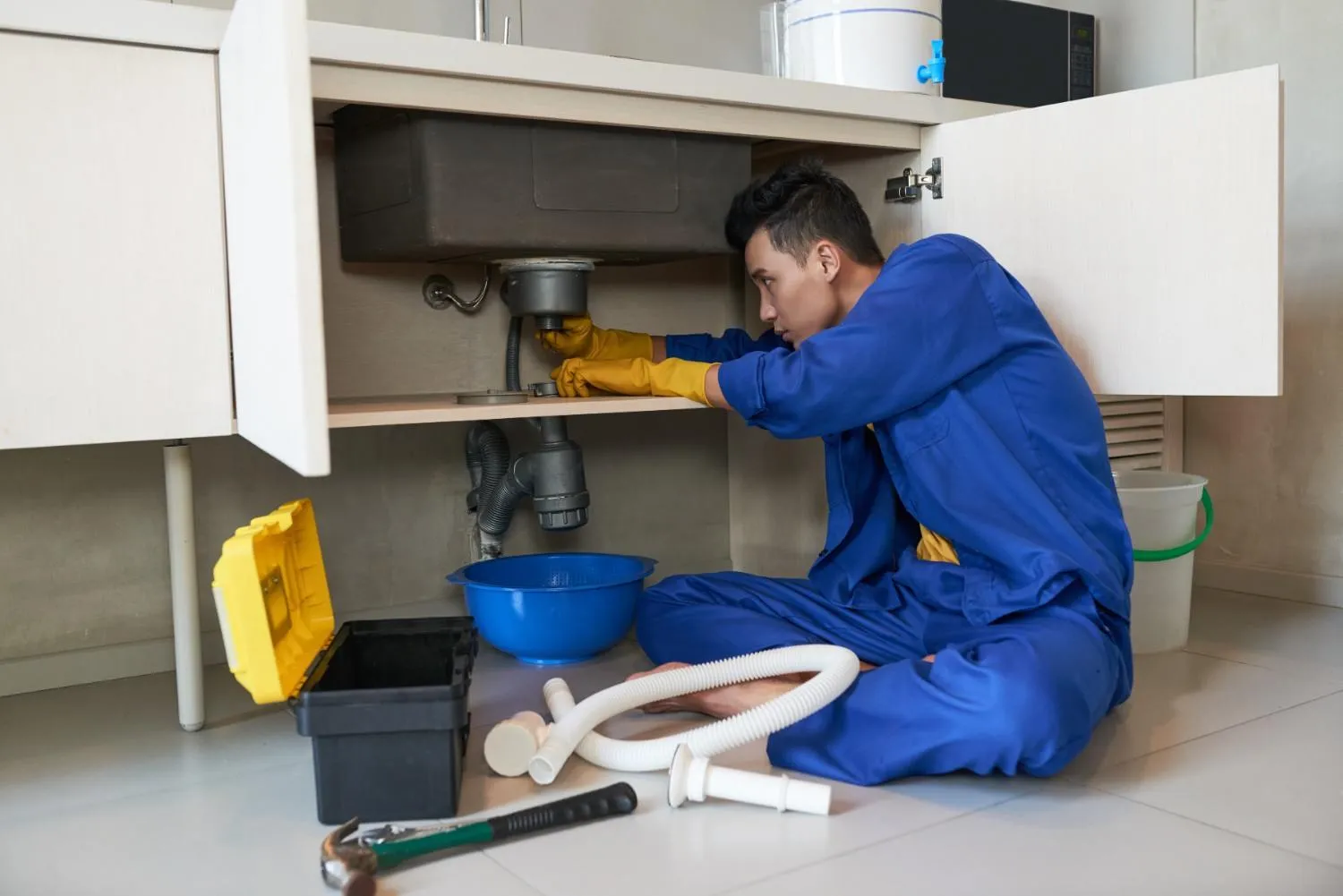 Plumber fixing pipes under a kitchen sink